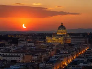 Visibilità dell'eclissi solare parziale sopra lo skyline di una città italiana al tramonto.